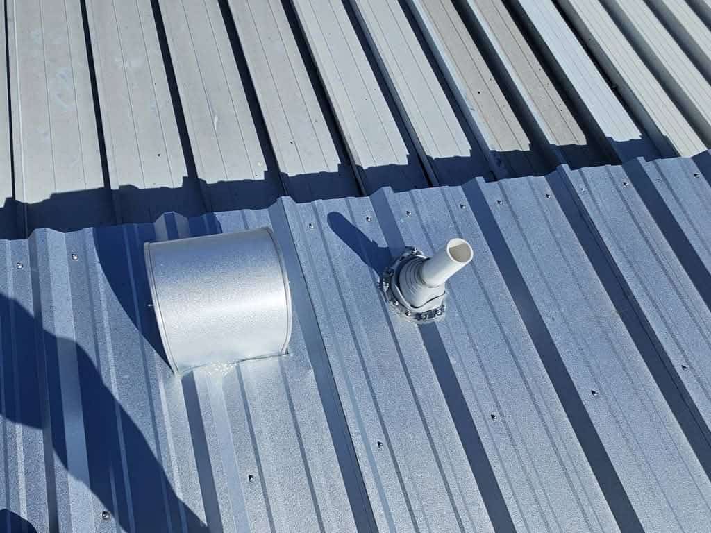 Close-up of a ribbed steel roof showing evenly spaced exposed fasteners, a sealed pipe boot and flashed roof penetration