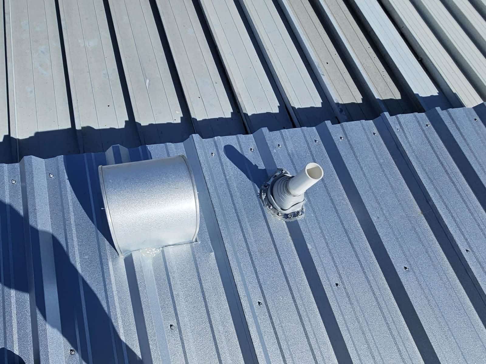 Close-up of a ribbed steel roof showing evenly spaced exposed fasteners, a sealed pipe boot and flashed roof penetration